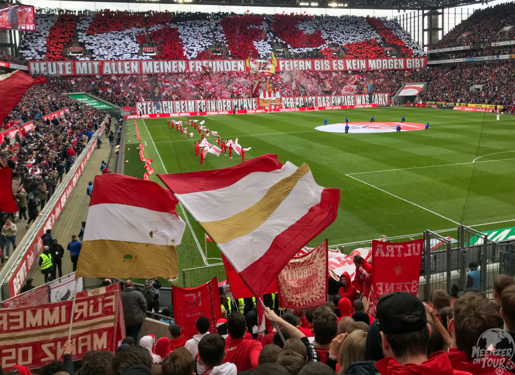 Fußballfans im Müngersdorfer Stadion mit Fahnen und einer Choreographie mit dem Logo des 1. FC Köln.