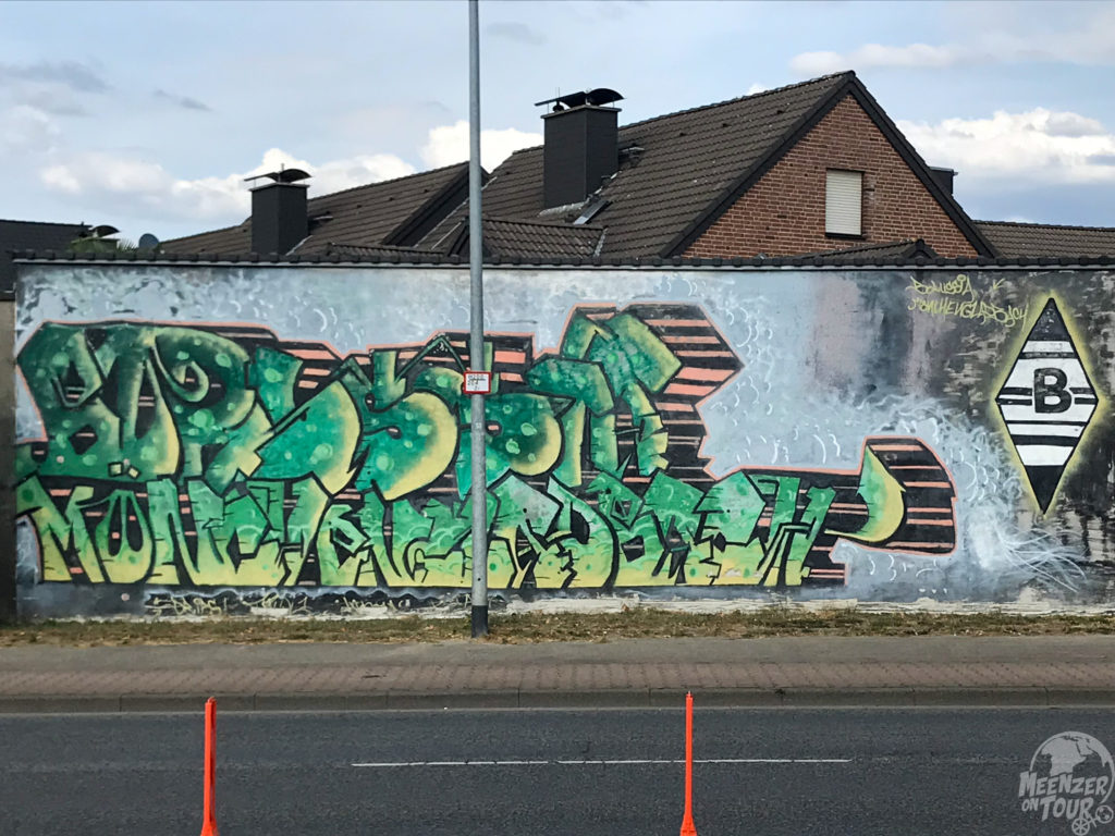 Borussia Mönchengladbach-Mural an einer Straße. Dahinter ein Backsteinhaus.